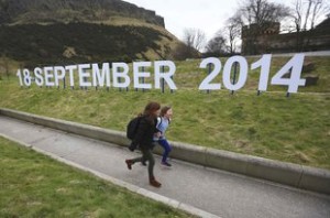 A teacher and schoolgirl run in front of a sign indicating the date of Scotland's independence referendum outside the Scottish Parliament in Edinburgh, Scotland